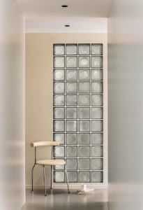 Modern minimalist living room featuring glass blocks on the wall, a sleek white chair, and books on the floor.