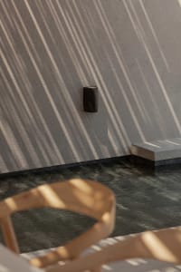 Modern minimalist outdoor pool with concrete walls and a black cylindrical light fixture casts abstract shadows on the wall.