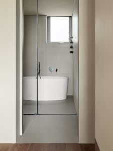 A modern minimalist bathroom with white walls and concrete floor and walls, featuring a white bathtub.