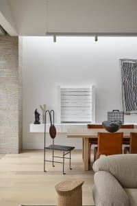 Modern dining room with wooden table, leather chairs, brick wall, and minimalist decor.