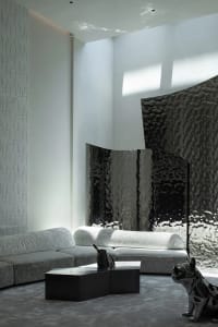 Modern interior design featuring taupe-colored fabric furniture, metallic accents, and a large window with a glass wall.