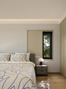 Modern minimalist bedroom featuring a bed with blue and white bedding and a side table with a lamp, set against a neutral col