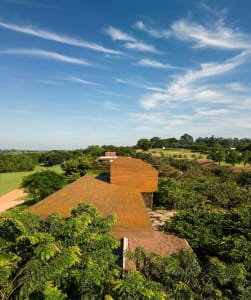 A modern house with a wooden roof and greenery surrounding it.