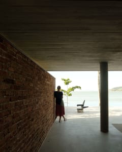 Person standing in a modern outdoor patio with brick walls and a concrete floor, overlooking the ocean.