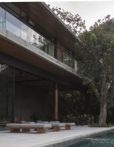 A modern residential exterior featuring a concrete and wooden structure, with a glass wall and a pool in the foreground.