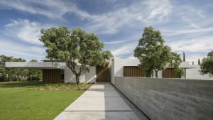A modern house with a concrete exterior and wooden accents surrounded by greenery.