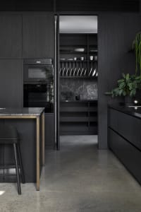 A modern, minimalist kitchen featuring dark wood cabinets, marble countertops, and concrete flooring.