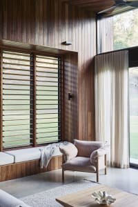 A modern living room featuring wooden furniture and large windows with wood-patterned blinds.