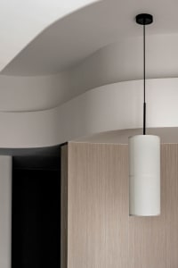 An image of a white cylindrical pendant light hanging from a curved ceiling in a minimalist interior design setting.