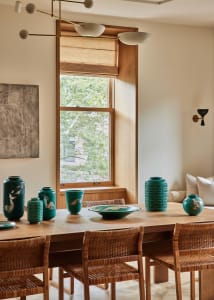 Modern dining room featuring a wooden table and chairs surrounded by turquoise ceramic vases and a large window.