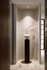 Ceramic vase with dried branches on a wooden pedestal in a minimalist interior design space.