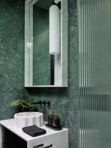 A modern bathroom with green marble walls, a glass shower enclosure, and black and white checkered floor tiles.