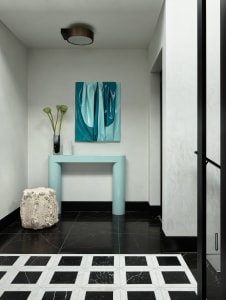 Modern lobby with minimalist design featuring a light green table, a unique white rock, and a teal painting.