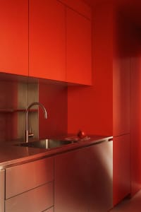 A minimalist kitchen featuring bright red walls, metallic countertops, and stainless steel sink.