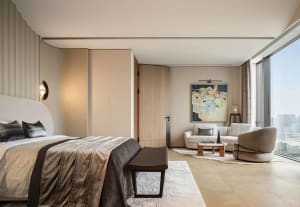 Modern bedroom featuring a bed with fabric bedding and wooden headboard, a small sofa, and a painting on the wall.