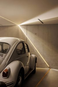 A white Volkswagen Beetle parked in a modern, minimalist concrete car parking space with linear lighting.