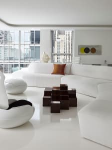 Modern, minimalist white lounge area with fabric seating and geometric coffee table, overlooking urban cityscape.