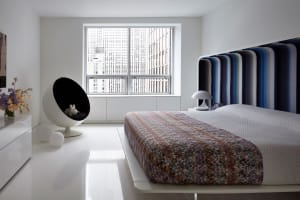 A minimalist bedroom featuring a modern bed with a colorful striped headboard and a sleek, white floor and furniture.