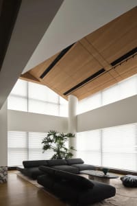 A modern living room with a dark sofa, large windows, and a large wooden ceiling.