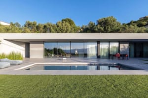 A modern house with a concrete exterior, featuring large glass windows and a swimming pool surrounded by green grass.
