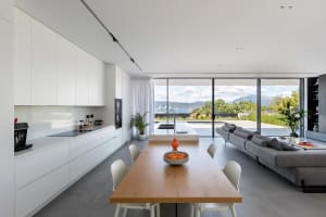 Contemporary kitchen with white cabinets and dark wood dining table, overlooking scenic outdoor view.