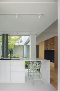 Modern minimalist kitchen with white cabinetry and open layout, featuring green bar stools and a large window overlooking a g