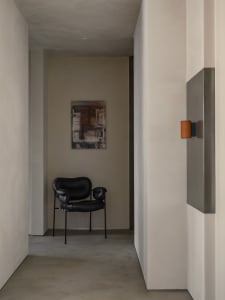 Modern interior design featuring a minimalist concrete wall with a sleek black armchair and a contemporary art piece.