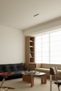 A modern living room with minimalist design, featuring a black leather sofa, a wooden coffee table, and a large window with a