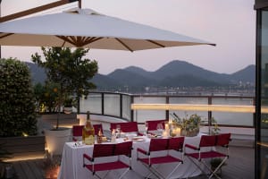 Outdoor dining setup with white tablecloth, red folding chairs, and evening sunset view.