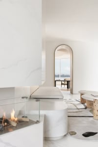 Modern minimalist living room featuring marble fireplace and furniture, with a view of a cityscape through an archway.