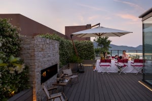 Outdoor dining area with family enjoying dinner at sunset, featuring wood deck, stone fireplace, and umbrella-covered dining 