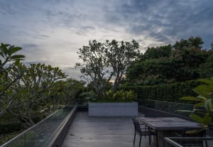 A rooftop patio featuring modern furniture, industrial plants, and wooden planters.