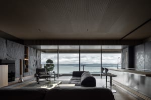 A modern minimalist living room featuring a concrete couch and glass walls overlooking a scenic view of the sea.