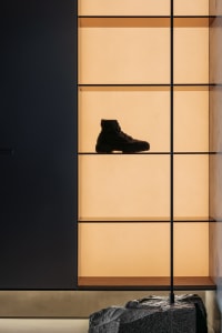 A minimalist retail space with glass walls displaying a single black boot on a shelf.