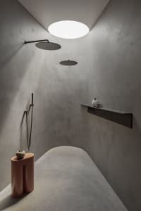A minimalist bathroom with concrete walls, two overhead showers, and a small shelf with decorative items.
