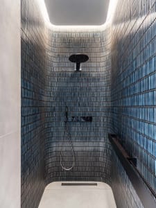 A minimalist bathroom with glass tiles, featuring a shower area with a ceiling light and a hand-held showerhead.
