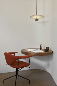 Modern home office setup with a round wooden table, orange chair, and pendant light.