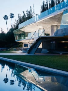 A modern residential building with glass and concrete exterior. Features include large windows, outdoor pool, and landscaping