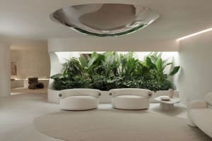 Modern interior design featuring white leather sofas and a circular coffee table with green plants in the background.