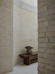 A minimalist interior space featuring a wooden bench with a woven basket on top.