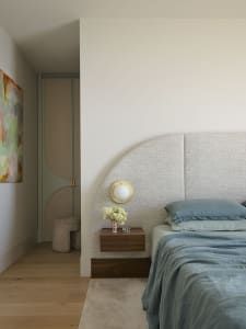 A modern bedroom featuring a bed with a textured fabric headboard, blue bedding, and a nightstand with a vase of flowers.