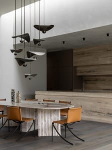 A modern dining room featuring a stone table and chairs with a unique abstract lighting fixture hanging above.