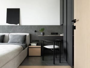 A minimalist bedroom featuring a bed with white bedding and a black headboard, accompanied by a small desk with a black chair
