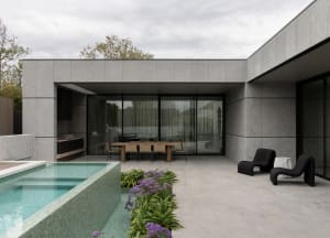 A modern, minimalist outdoor living area featuring a concrete swimming pool and deck with contemporary furniture.
