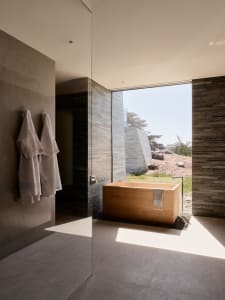 A modern bathroom featuring a wooden bathtub surrounded by concrete tiles and natural light.