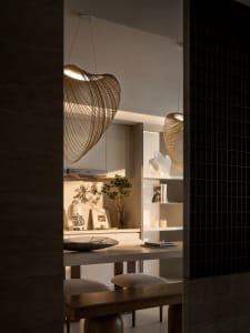 Modern minimalist kitchen with wooden tables and chairs, glass pendant lights, and white cabinets.