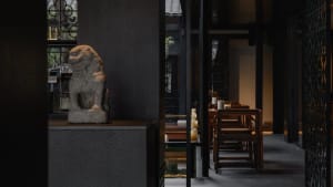 A modern restaurant interior featuring a stone lion statue and dark furnishings.