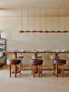 Modern restaurant interior with wooden tables and stools, minimalist design, and pendant lighting.