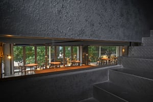 Industrial-style cafe with metal tables and chairs, large windows, and concrete walls.
