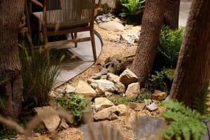 A modern outdoor garden featuring natural stones and gravel, with a comfortable seating area surrounded by trees and greenery